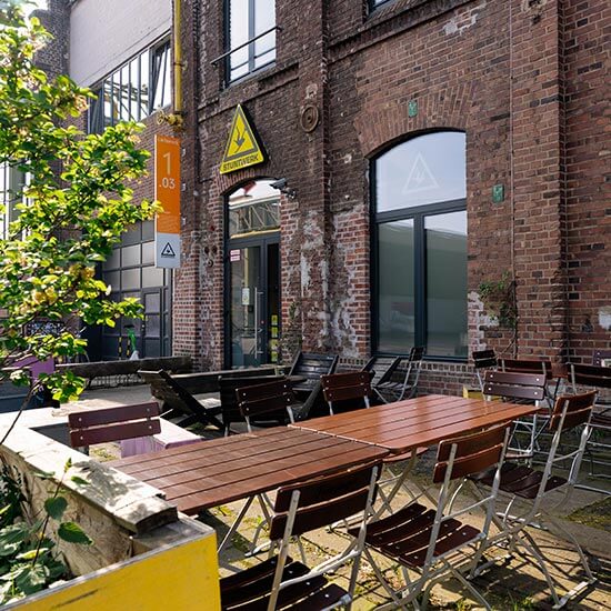 Gemütlicher Außenbereich des Stuntwerk Köln Mülheim mit vielen Sitzgelegenheiten durch Bistrotische.
