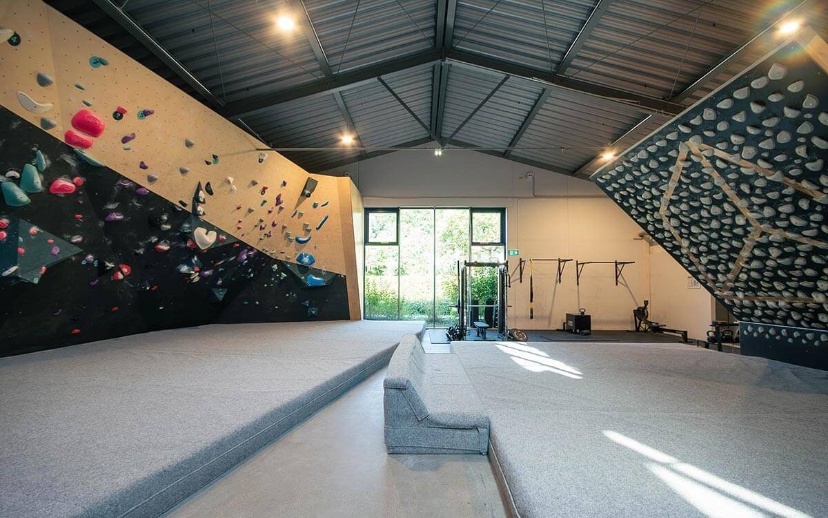 Helle Boulderhalle mit schwarzen und beigen Wänden, bunten Klettergriffen in Pink, Blau und Weiß sowie großzügiger Fensterfront im Stuntwerk Trostberg.