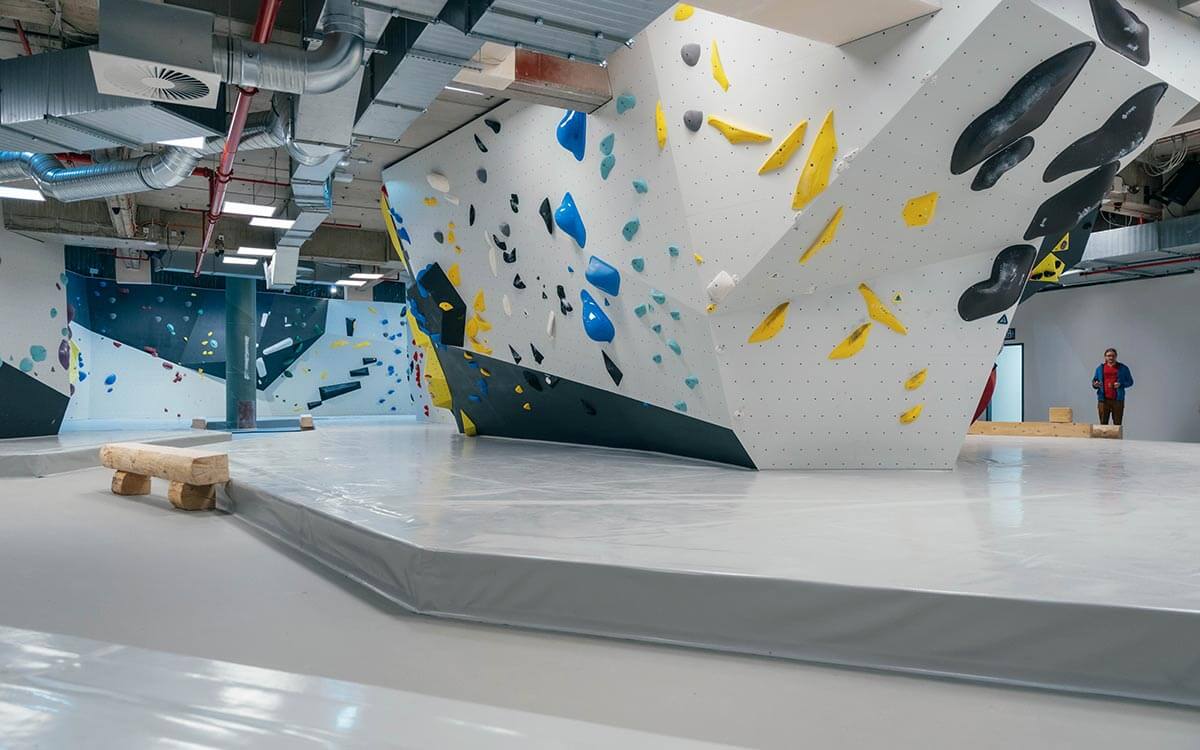 Helle Boulderfläche im Stuntwerk Troisdorf mit grauer Wand, bunten Griffen und geometrischen Formen. Optimale Trainingsfläche für Einsteiger und Fortgeschrittene.