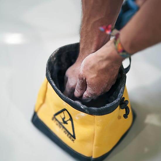 Hände greifen in einen gelben Chalkbag mit Stuntwerk-Logo, um die Finger mit Magnesium für das Bouldern zu bestäuben.