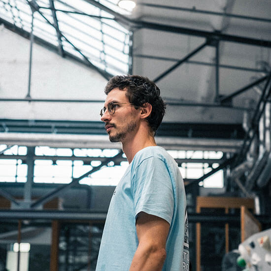Junger Mann steht seitlich in der Boulderhalle und schaut aufmerksam in eine Richtung.