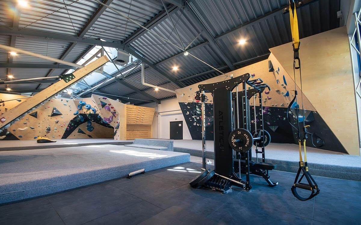 Großer Trainingsbereich mit schwarzem Fitnessrack, TRX-Bändern und Boulderwänden in Beige und Schwarz mit bunten Griffen im Stuntwerk Trostberg.