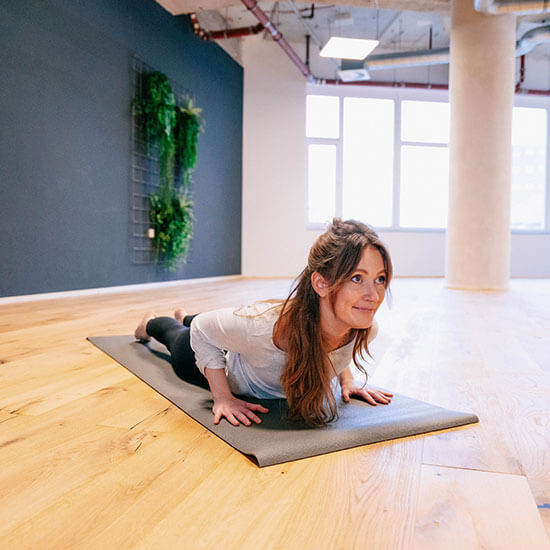 Frau in weißem Shirt und schwarzer Leggings macht im hellen Yoga-Studio des Stuntwerks die Kobra-Pose. Der Fokus liegt auf Ruhe, Atmung und Körperbewusstsein.