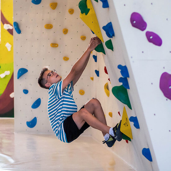 Jugendlicher klettert konzentriert an einer bunten Boulderwand im Kinder- und Jugendbereich des Stuntwerks Senden. Die Wand ist mit gelben, grünen, blauen und violetten Griffen gestaltet – ein lebendiger Ort voller Energie, Spaß und Bewegung.