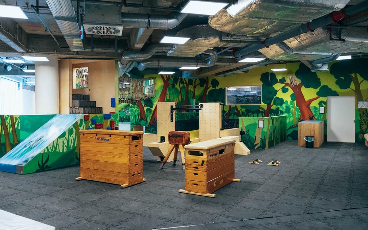 Heller Indoor-Kinderbereich mit Turngeräten, Holz-Kästen und farbenfroher Dschungelmalerei im Stuntwerk Troisdorf. Perfekt für Parkour- und Bewegungstraining für Kinder.