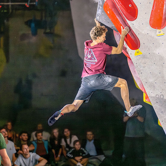 Athlet springt an roter Boulderwand beim Stuntmoves Finale. Kraft, Dynamik und Spannung – das Publikum fiebert mit.