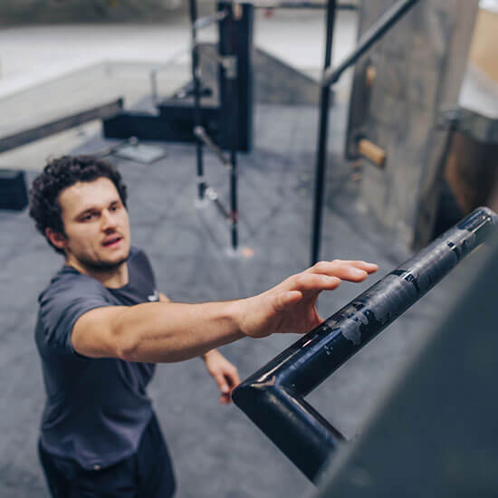 Sportler greift im Parkourtraining nach einer Metallstange und fokussiert den nächsten Move