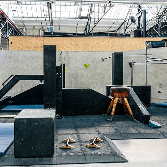 Moderner Parkourbereich mit verschiedenen schwarzen Hindernissen, Matten und Turnpferd in heller Industriehalle