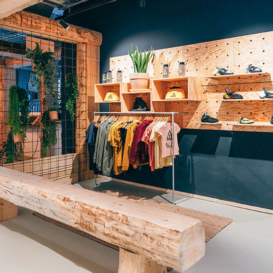 Übersicht des Stuntwerk-Shops mit Holzregalen, Boulder-Equipment, Shirts und Accessoires. Natürliche Materialien und warme Farben schaffen eine gemütliche Atmosphäre.