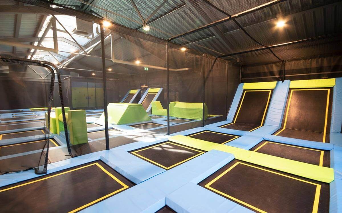 Große Indoor-Trampolinhalle mit blauen und gelben Sprungflächen, schwarzen Trampolinen und grünen Hindernissen im Stuntwerk Trostberg.