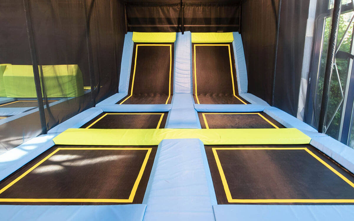 Große Indoor-Trampolinhalle mit blauen und gelben Sprungflächen, schwarzen Trampolinen und grünen Hindernissen im Stuntwerk Trostberg.